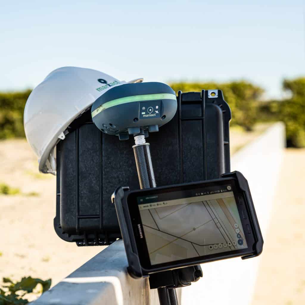 GNSS-ontvanger op een paal met tablet met kaart, een veiligheidshelm en zwarte koffer op een laag muurtje