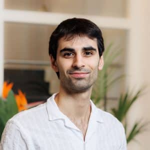 Portret van een man met donker haar in wit overhemd voor planten met oranje bloemen