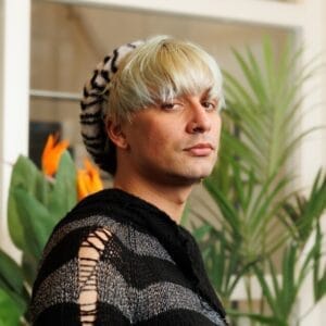 Portret van persoon met blonde pony en gebreide trui voor planten en oranje bloemen