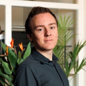 Portret van een jonge man met kort bruin haar in donkergroen overhemd voor planten met oranje bloemen