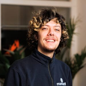 Lachende man met donker krullend haar in donkerblauw vest met marXact-logo voor kantoorplanten