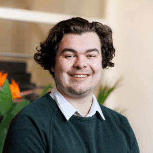 Portret van een lachende man met donker krullend haar in groene trui over wit overhemd in een licht kantoor