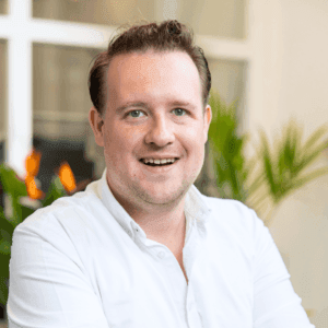 Portret van een lachende man met kort blond haar in wit overhemd voor kantoorplanten