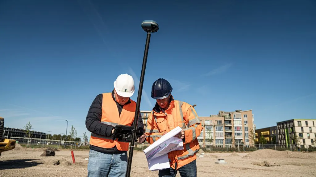 Two site workers checking a drawing next to a UNI-GR2 on a survey pole