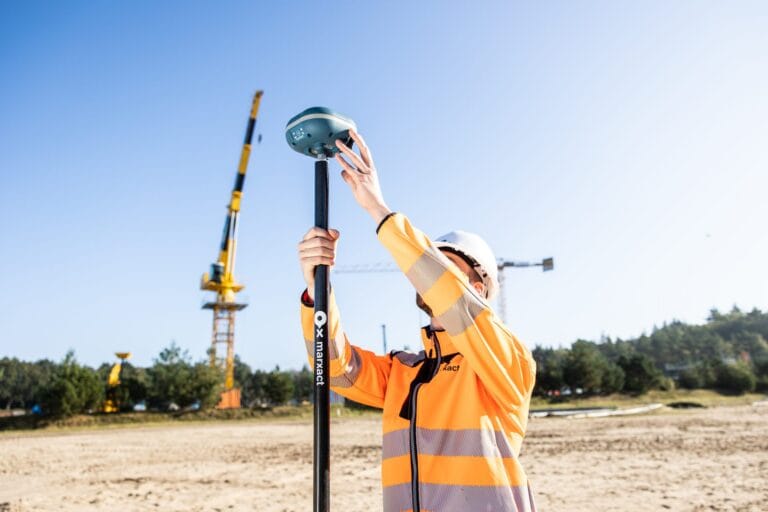 Site worker placing a marXact UNI-GR2 GNSS receiver on a survey pole on a construction site