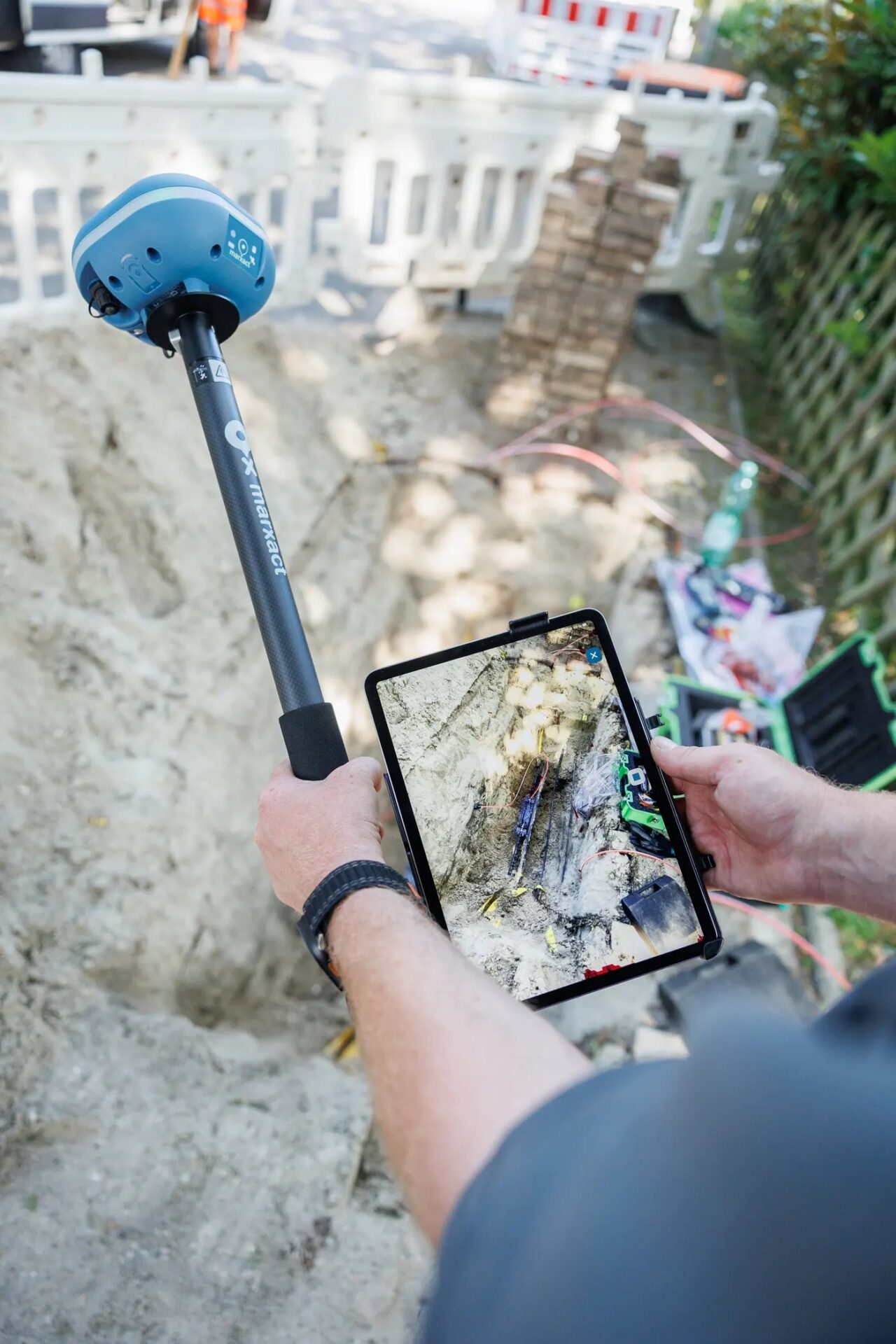 UNI-GR2 on a survey pole next to an iPad Pro showing a 3D recording of an open trench with cables