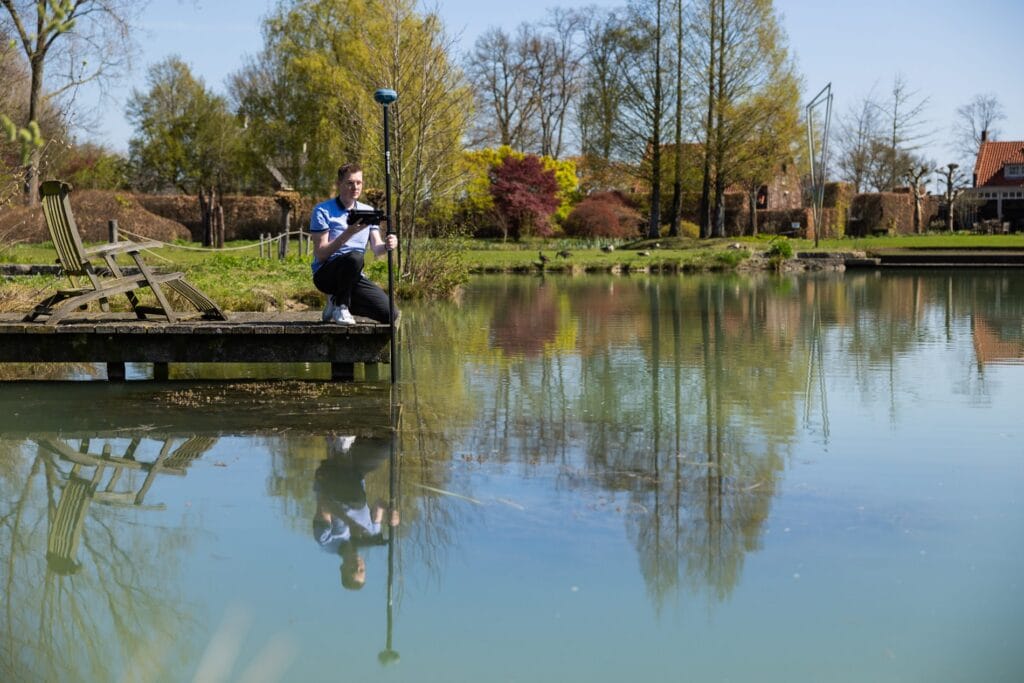 Landscaper with a UNI-GR2 pole in the pond from a jetty, trees reflected in the water