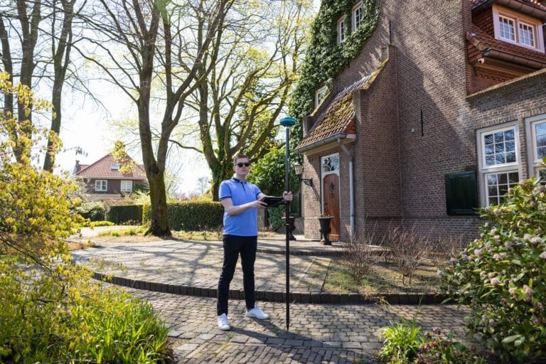 Landscaper with a UNI-GR2 on a pole and tablet on a brick path beside a brick villa