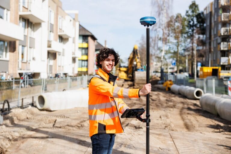 Surveyor with a UNI-GR2 and tablet on a dug-up street with concrete pipes and a yellow excavator