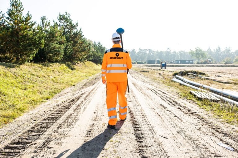 Surveyor in orange marXact workwear walks down a sandy track with a UNI-GR2 on his shoulder