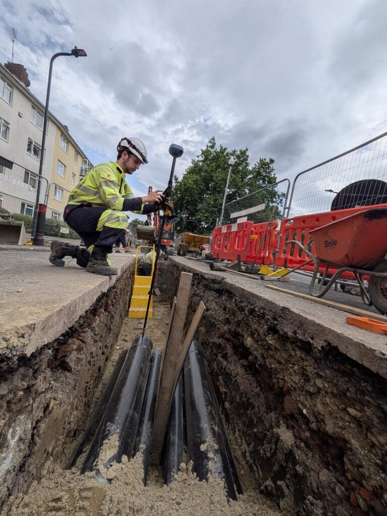 Deep trench with black cable ducts, worker with UNI-GR2 crouching at the edge