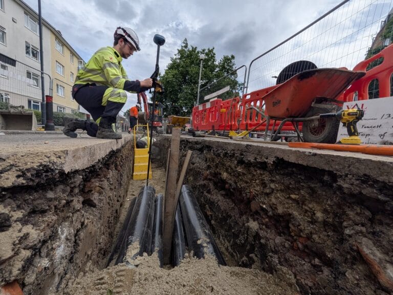 Wide shot of a trench with cable ducts, worker with UNI-GR2 and flats in the background