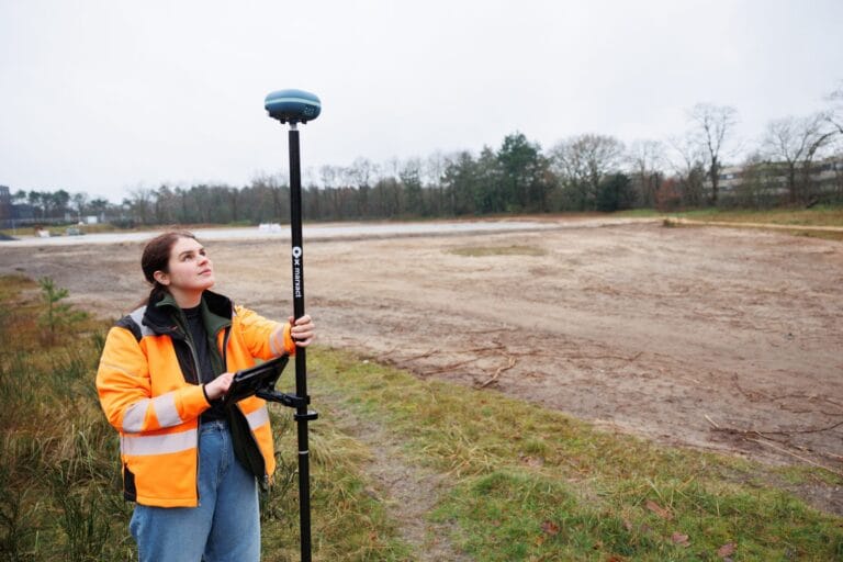 Surveyor looks up at the UNI-GR2 receiver, controller in hand, on a sand plot