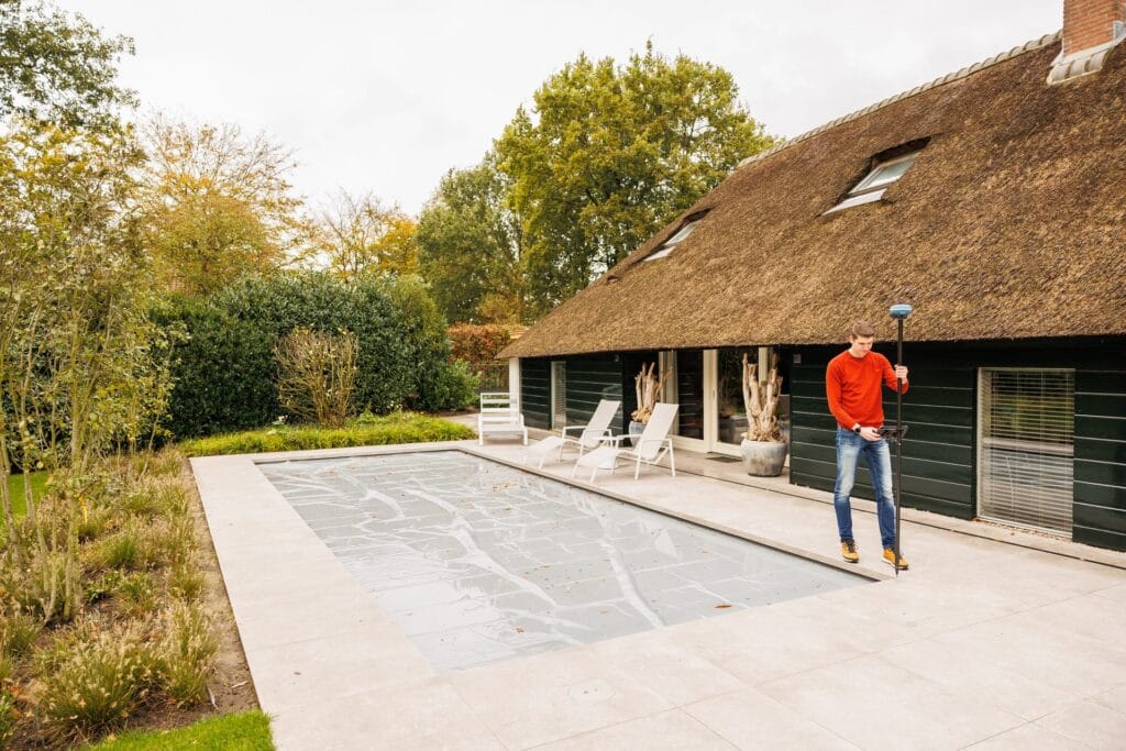 Wide view of a garden with pool and thatched house, a man with UNI-GR2 in the background