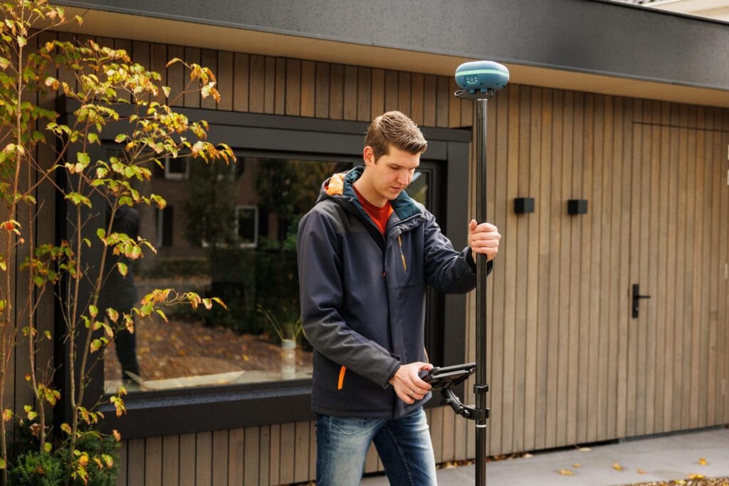 Man with UNI-GR2 and tablet measures beside a timber-clad garden building with large window