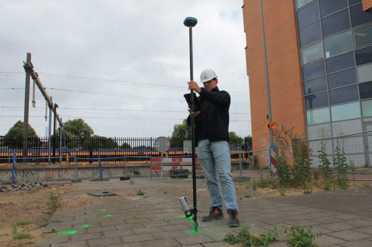 Worker with UNI-GR2 pole beside an office building, a row of green dots on the paving towards the railway
