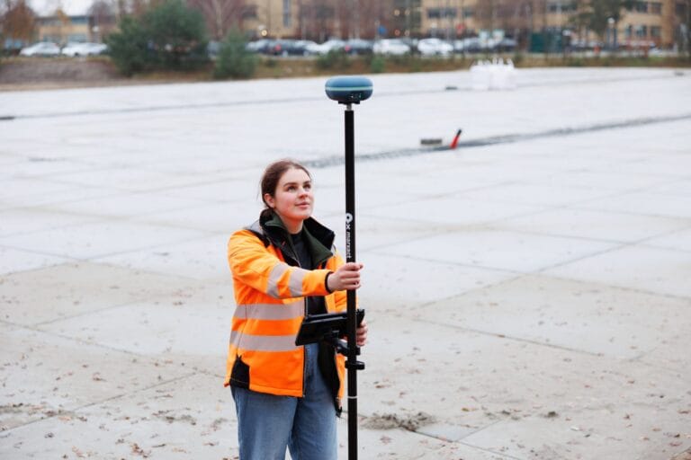 Surveyor in an orange jacket looks up at the UNI-GR2 receiver on a paved area