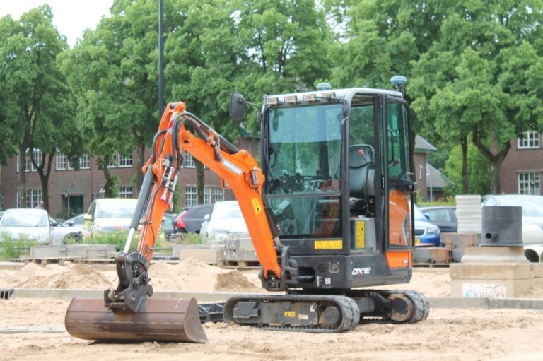 Orange mini excavator with GNSS antennas on the cab stands on a sand site